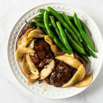 sliced apples and chicken with green beans on a white plate.