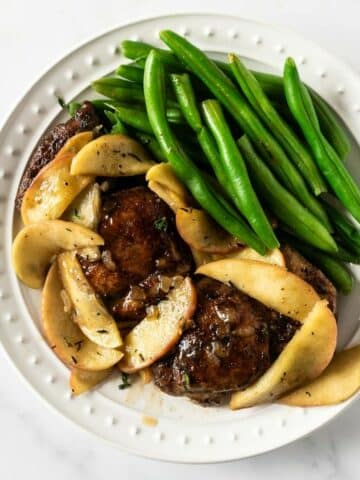 sliced apples and chicken with green beans on a white plate.