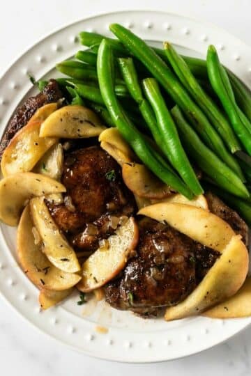 sliced apples and chicken with green beans on a white plate.