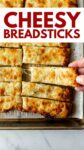 breadsticks on a baking sheet with overlay text "cheesy breadsticks".