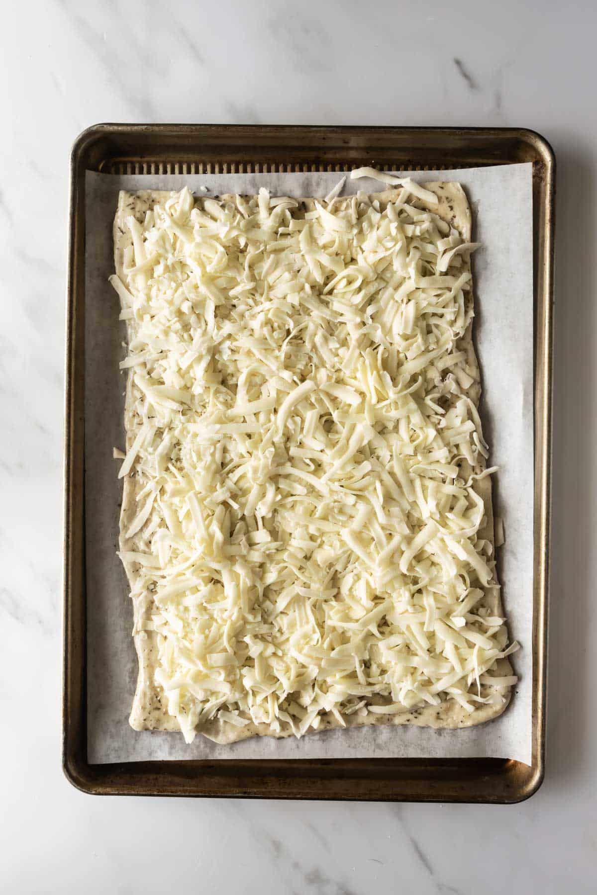 pizza dough topped with shredded cheese on a baking sheet.