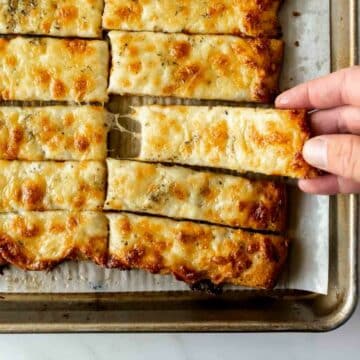 reaching for cheesy breadsticks on a baking sheet.