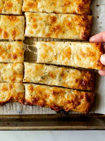 reaching for cheesy breadsticks on a baking sheet.