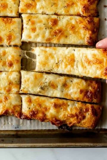 reaching for cheesy breadsticks on a baking sheet.