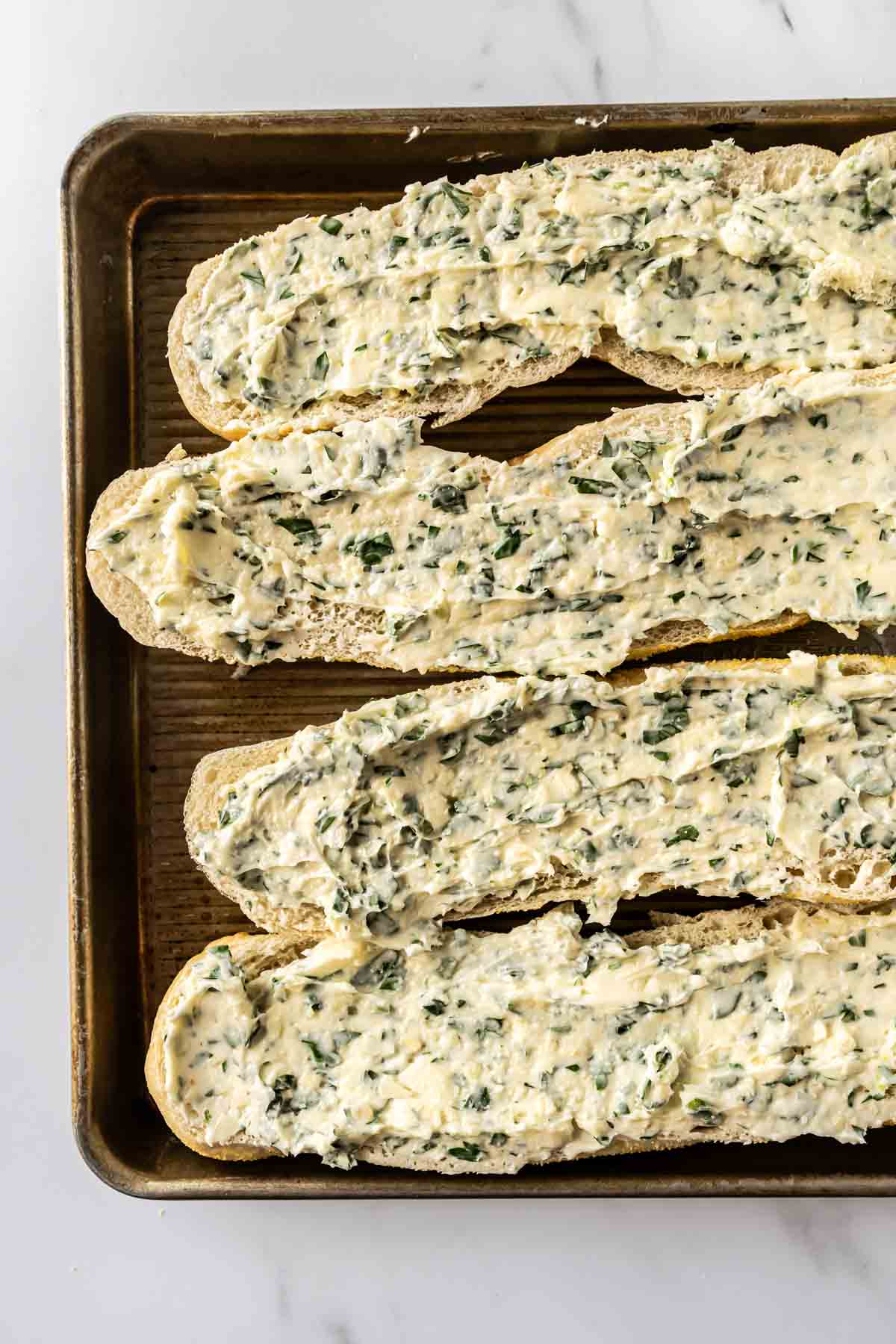 4 pieces of French bread topped with herb butter on a baking sheet.