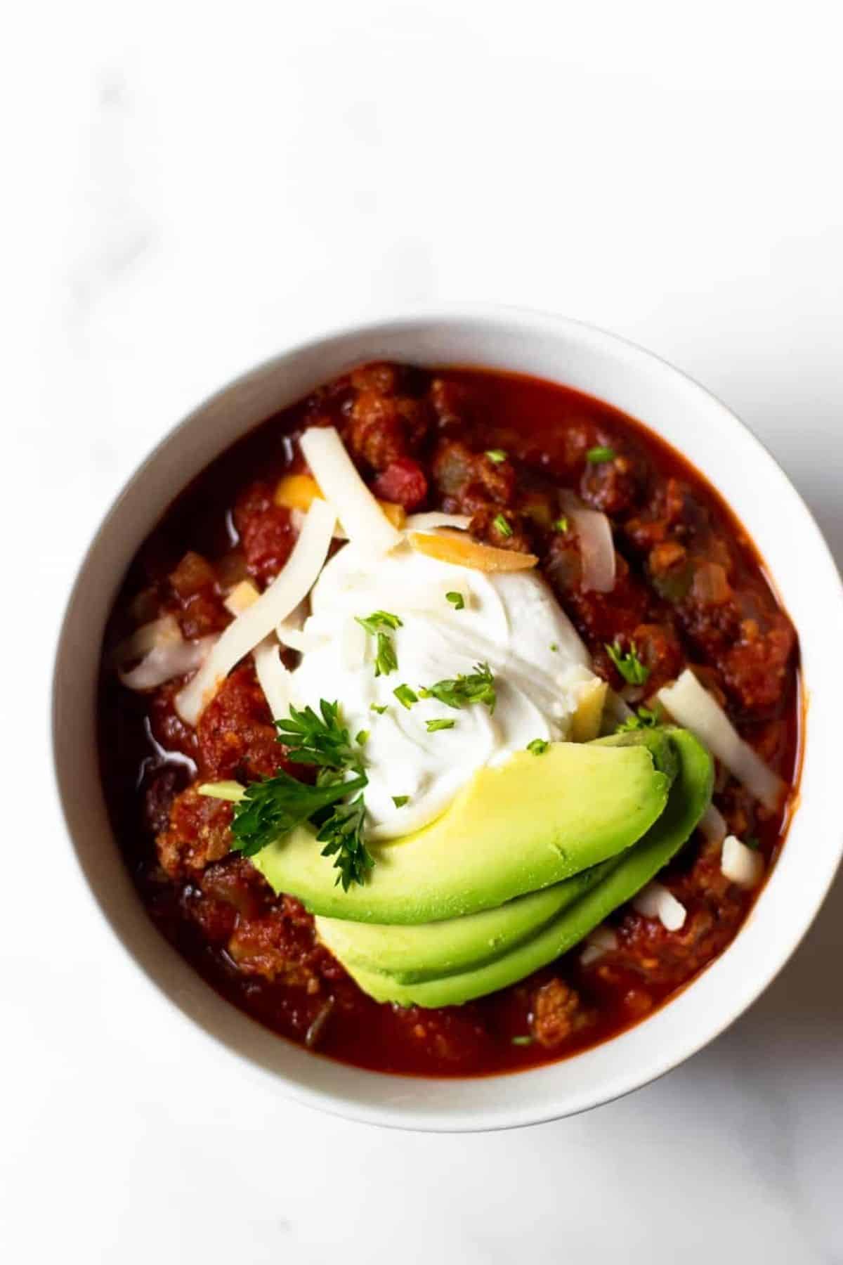 chili in a bowl topped with cheese, sour cream, and avocado.