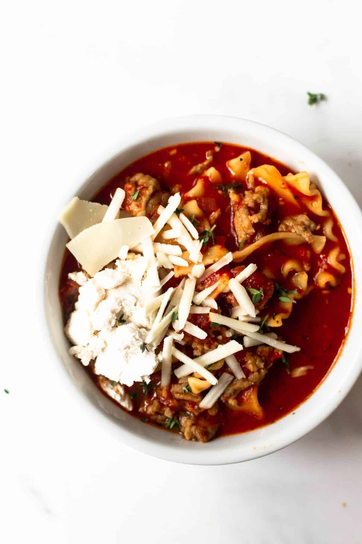 lasagna soup in a white bowl topped with ricotta and shredded cheese.