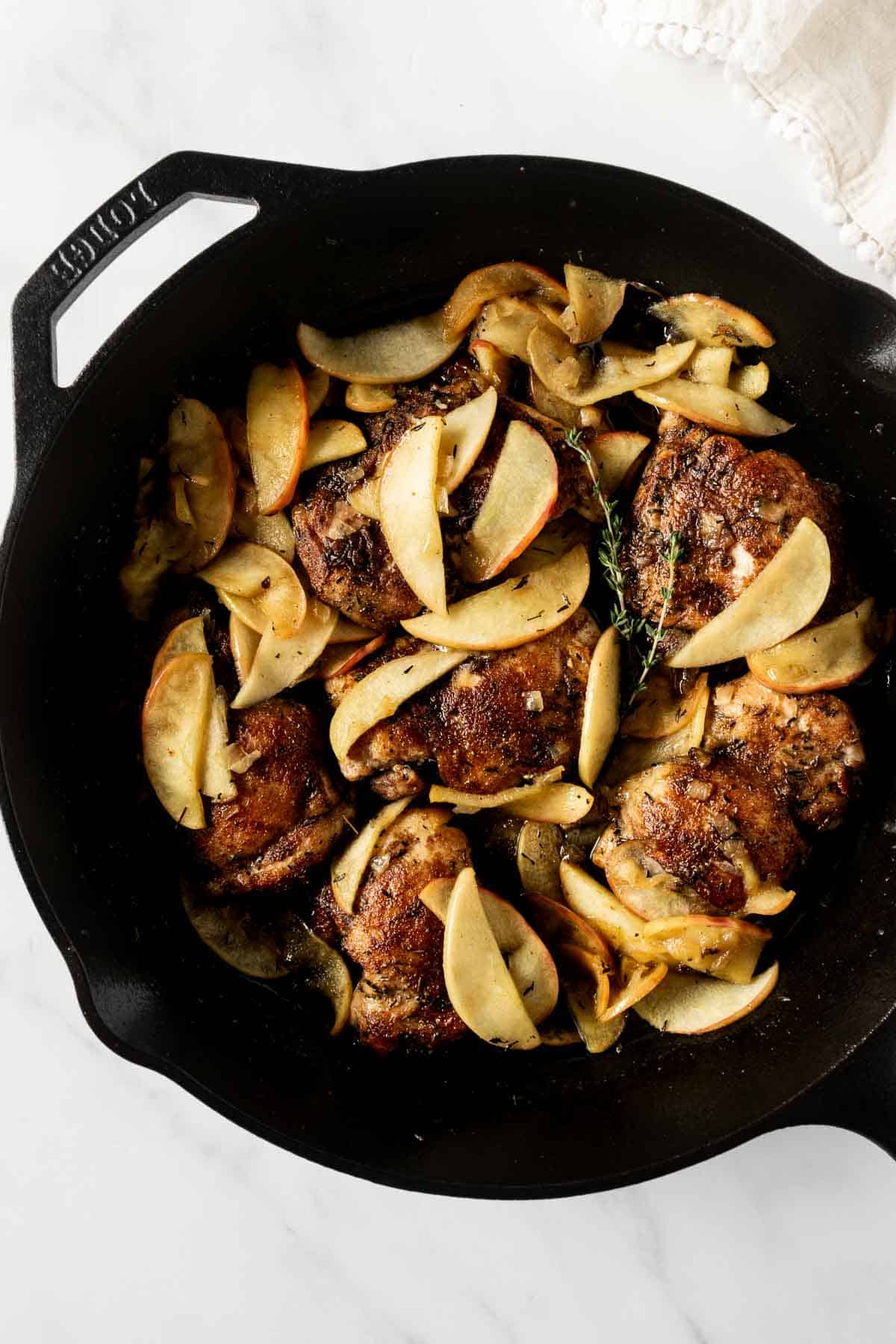 chicken with sliced apples and cider pan sauce in a cast iron pan.