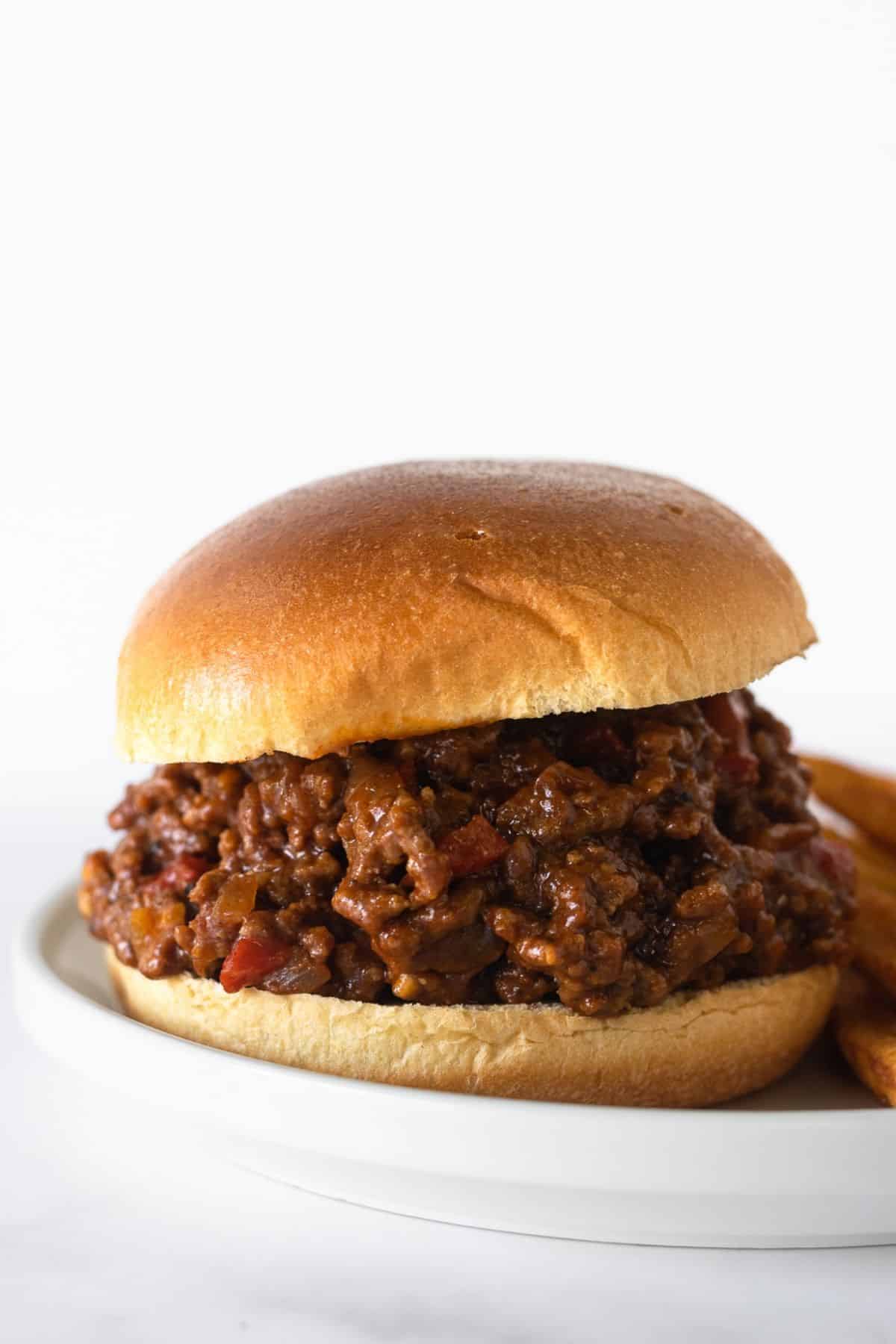 sloppy joe meat in a burger bun on a white plate.