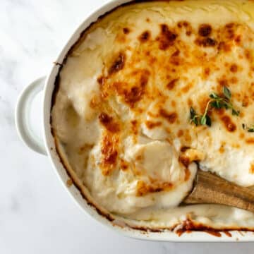 scalloped potatoes in a white baking dish with a wooden spoon.