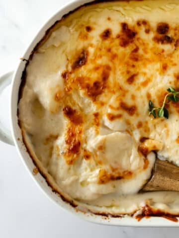 scalloped potatoes in a white baking dish with a wooden spoon.