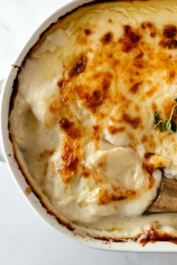 scalloped potatoes in a white baking dish with a wooden spoon.