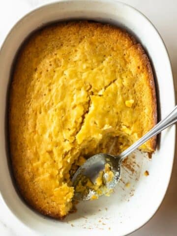 corn casserole in a white baking dish with a spoon.