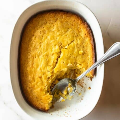 corn casserole in a white baking dish with a spoon.