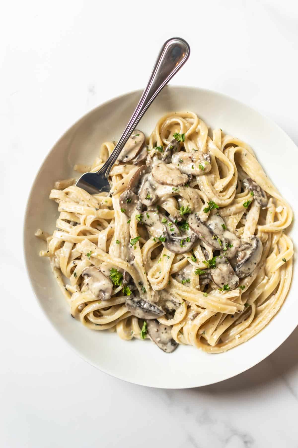 mushroom pasta with a fork in a white bowl.