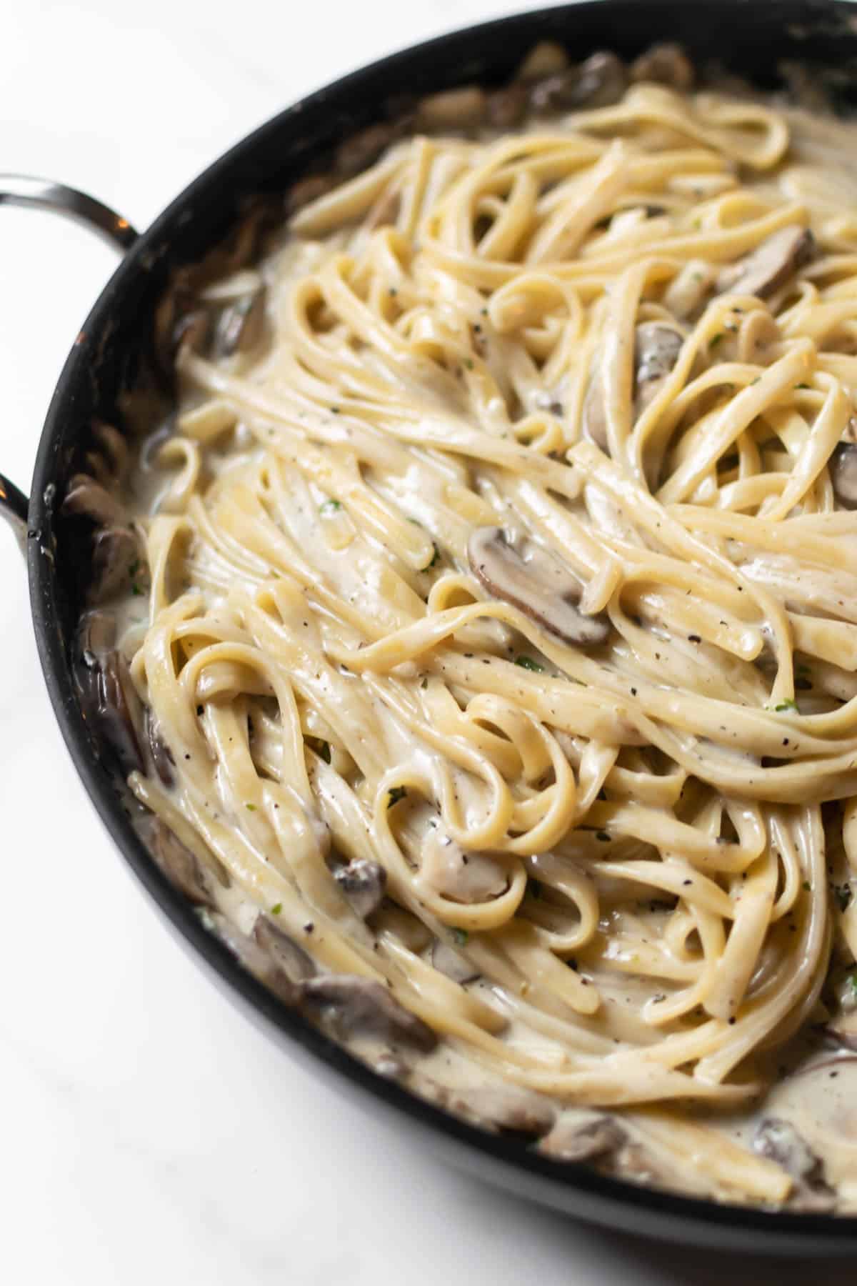 pasta with mushrooms in a cream sauce in a black skillet.