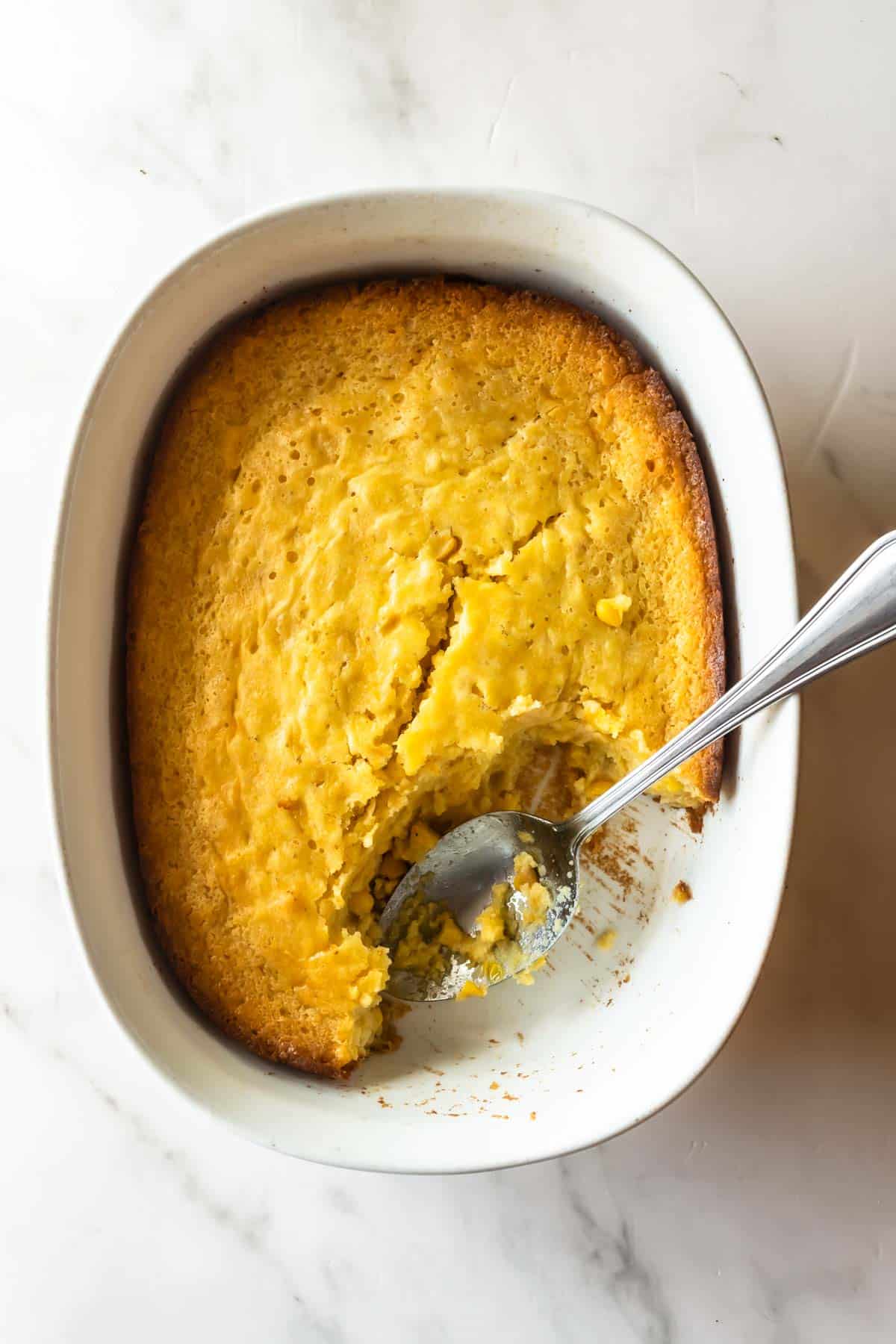 cornbread casserole in a white baking dish with a spoon.