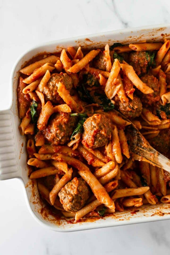 baked penne pasta in a white baking dish with a spoon.