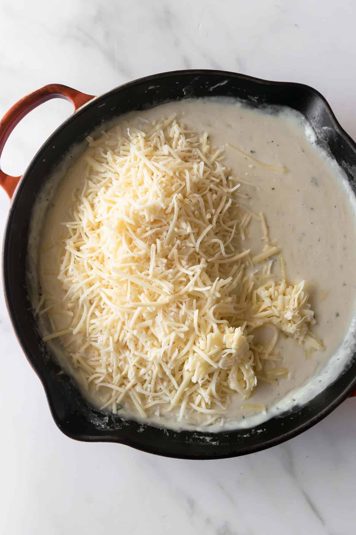 cream sauce with shredded cheese in a skillet.