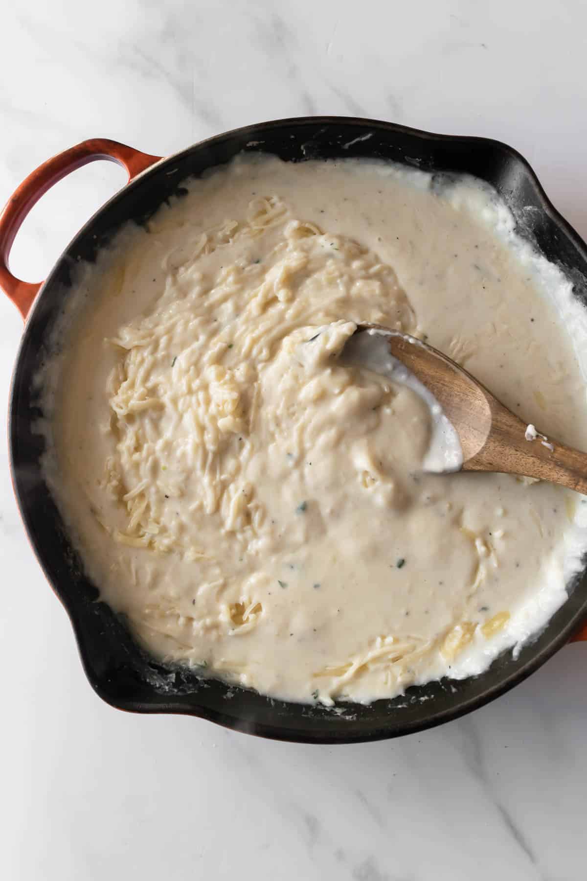 cheese cream sauce in a skillet with a wooden spoon.