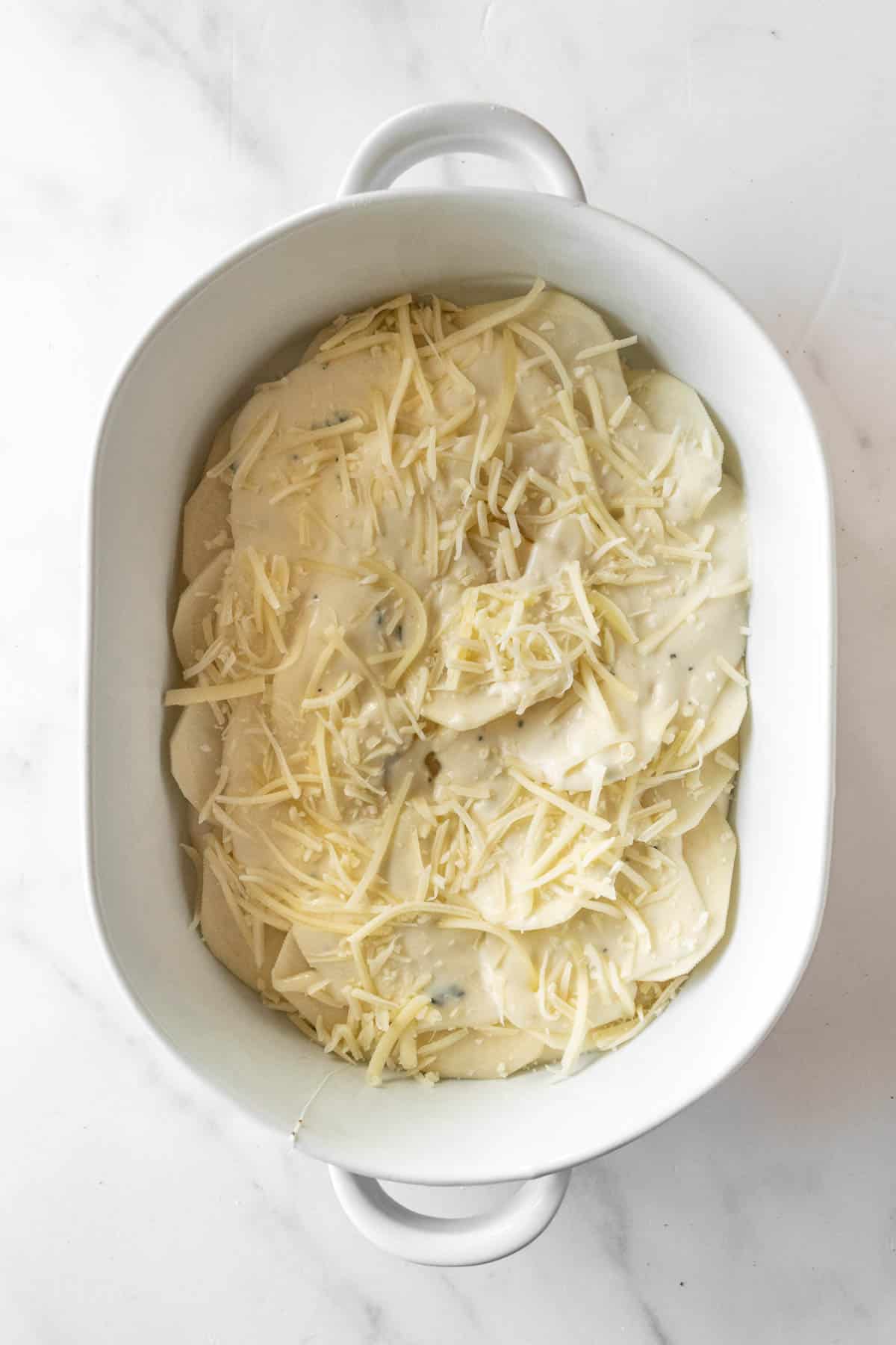 sliced potatoes covered in cheese in a white baking dish.