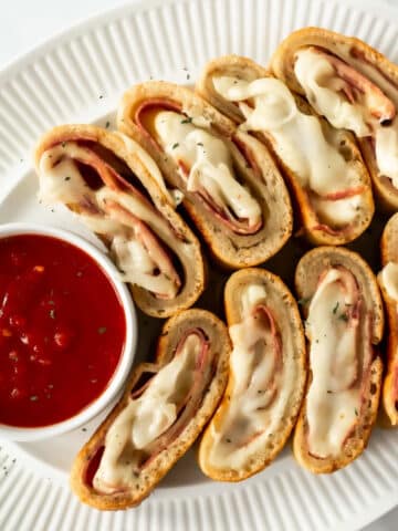 slices of homemade stromboli on a white plate with a cup of marinara sauce.