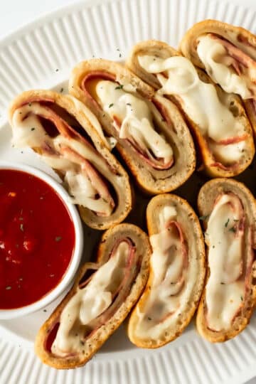 slices of homemade stromboli on a white plate with a cup of marinara sauce.