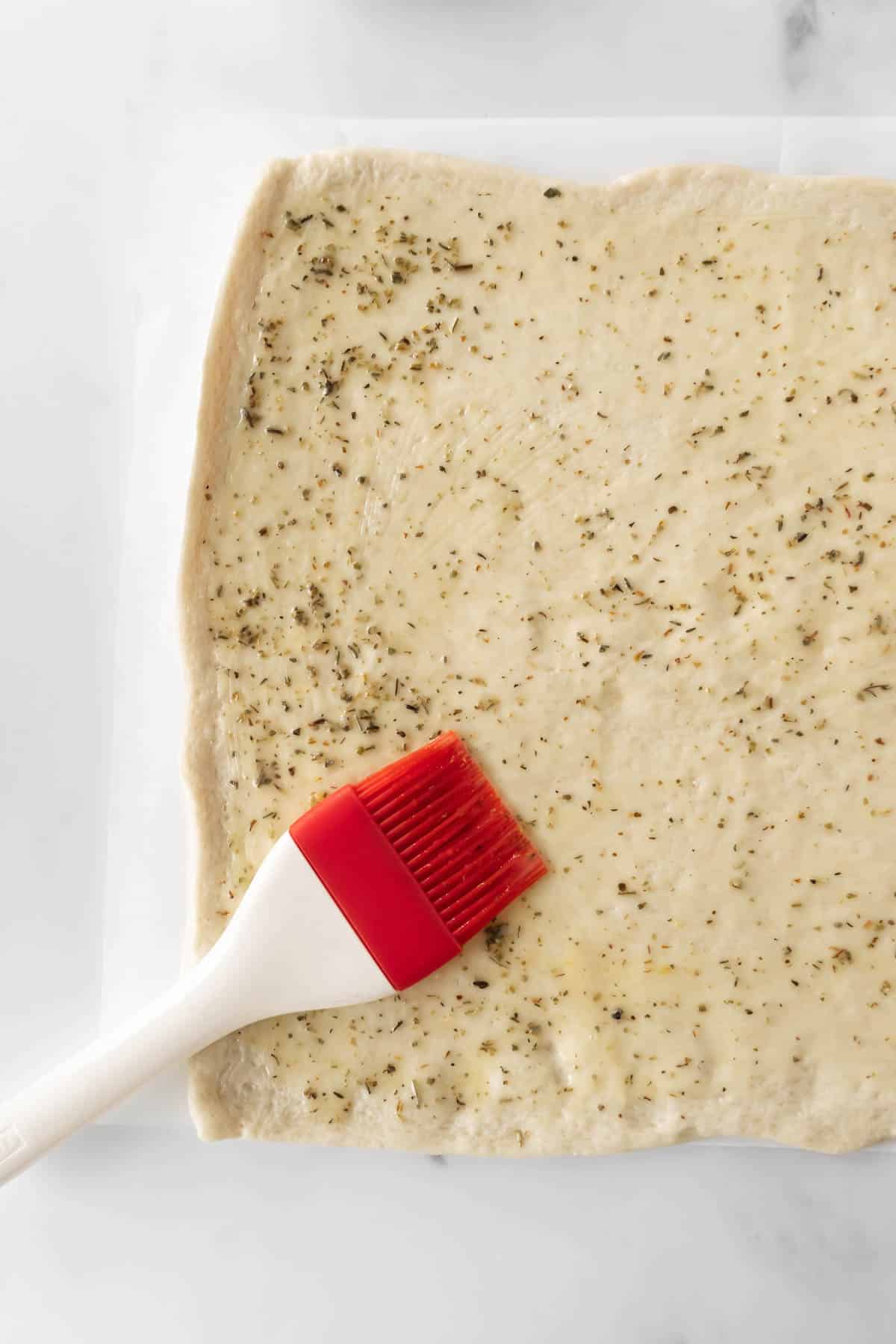 brushing melted herb butter onto pizza dough.