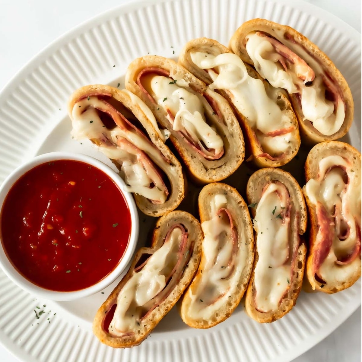 slices of homemade stromboli on a white plate with a cup of marinara sauce.