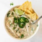 chicken chili recipe in a white bowl topped with cilantro, jalapeños, and chips.