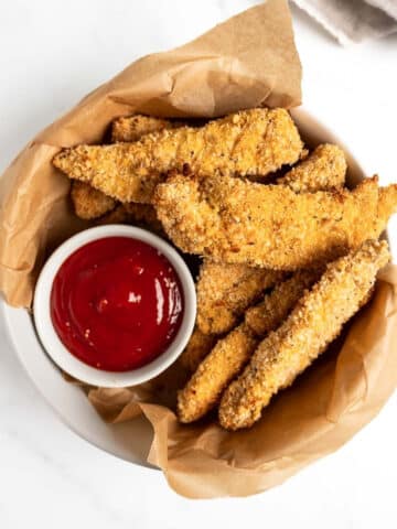 baked chicken tenders in a bowl with ketchup.