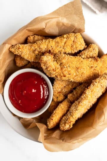 baked chicken tenders in a bowl with ketchup.