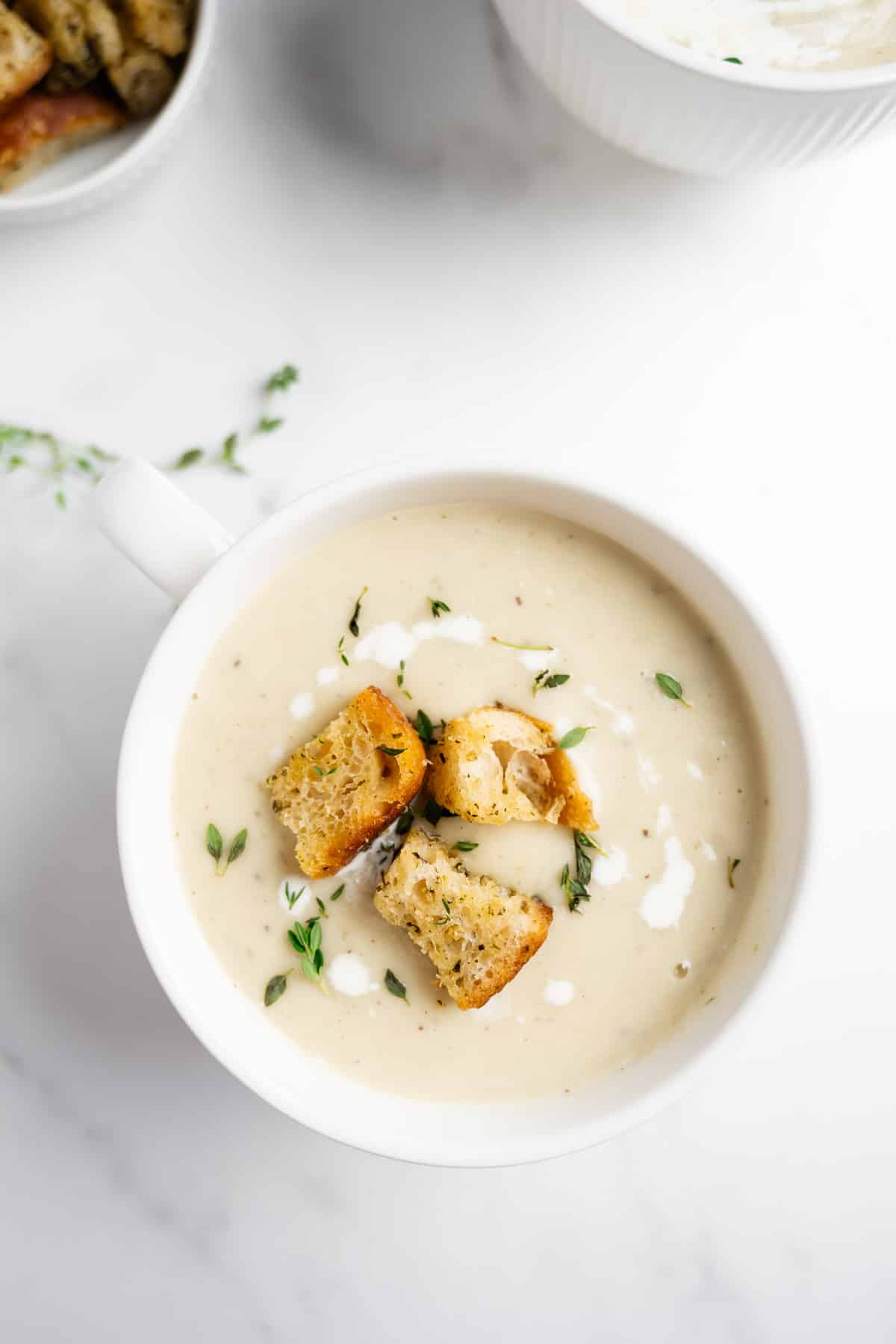 creamy cauliflower and potato soup in a white bowl with a handle.