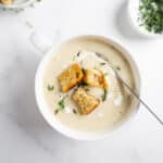 creamy cauliflower potato soup in a white bowl with a spoon.