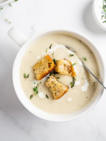 creamy cauliflower potato soup in a white bowl with a spoon.