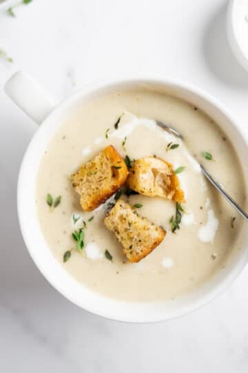 creamy cauliflower potato soup in a white bowl with a spoon.