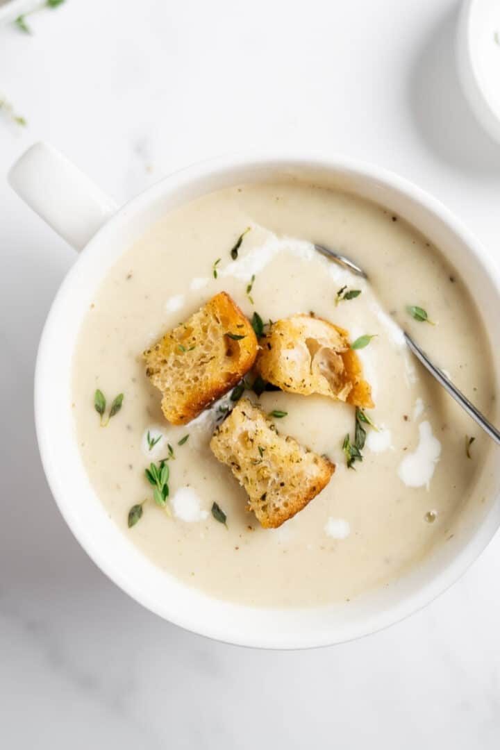 creamy cauliflower potato soup in a white bowl with a spoon.