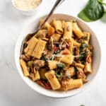 creamy tuscan pasta recipe in a bowl with a fork on a white table topped with cheese.