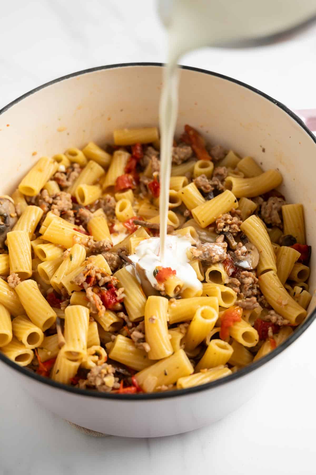 pouring heavy cream into a pot of pasta.