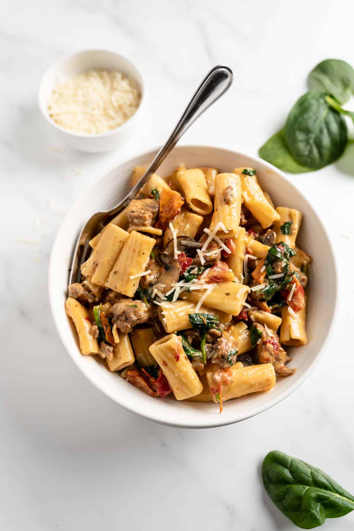 creamy tuscan sausage pasta in a white bowl with a fork.