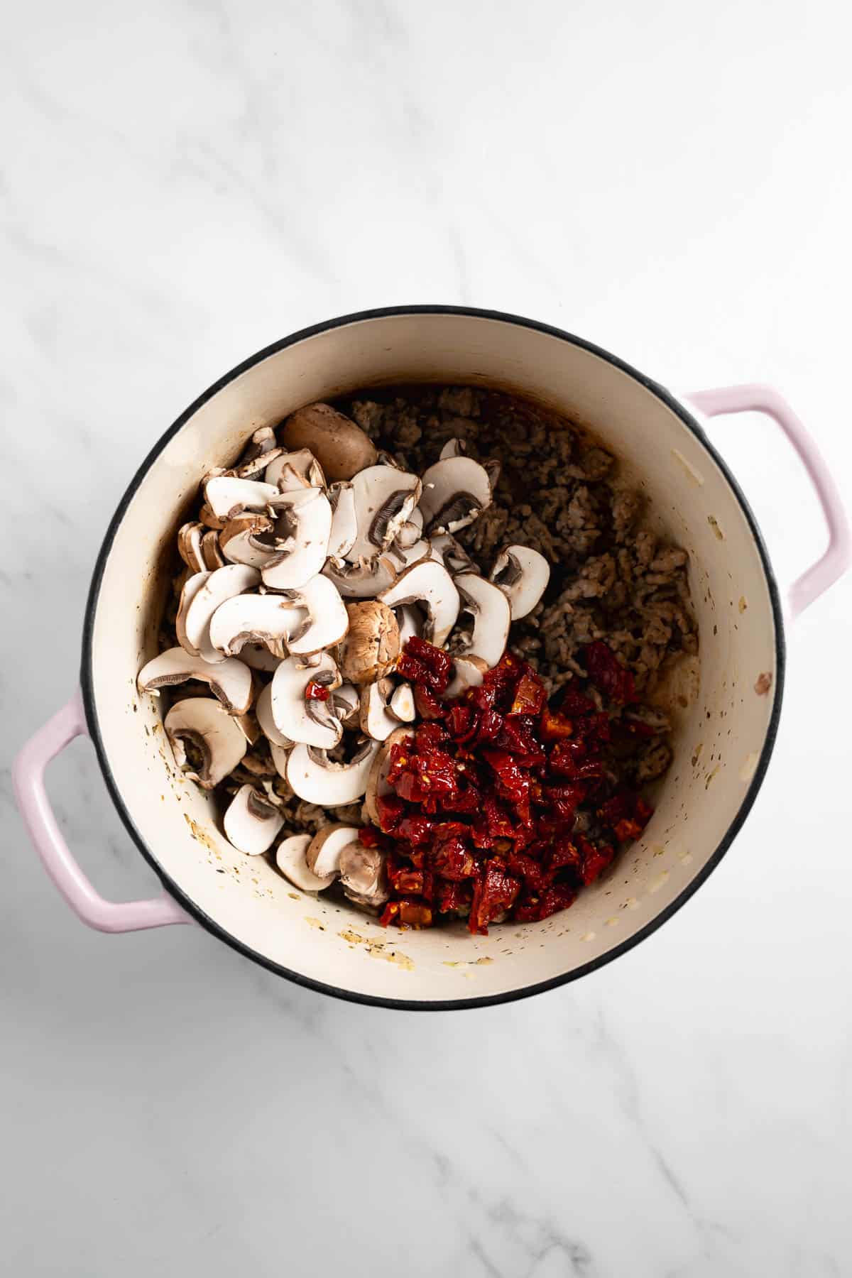 ground sausage topped with mushrooms and sun dried tomatoes in a pot.