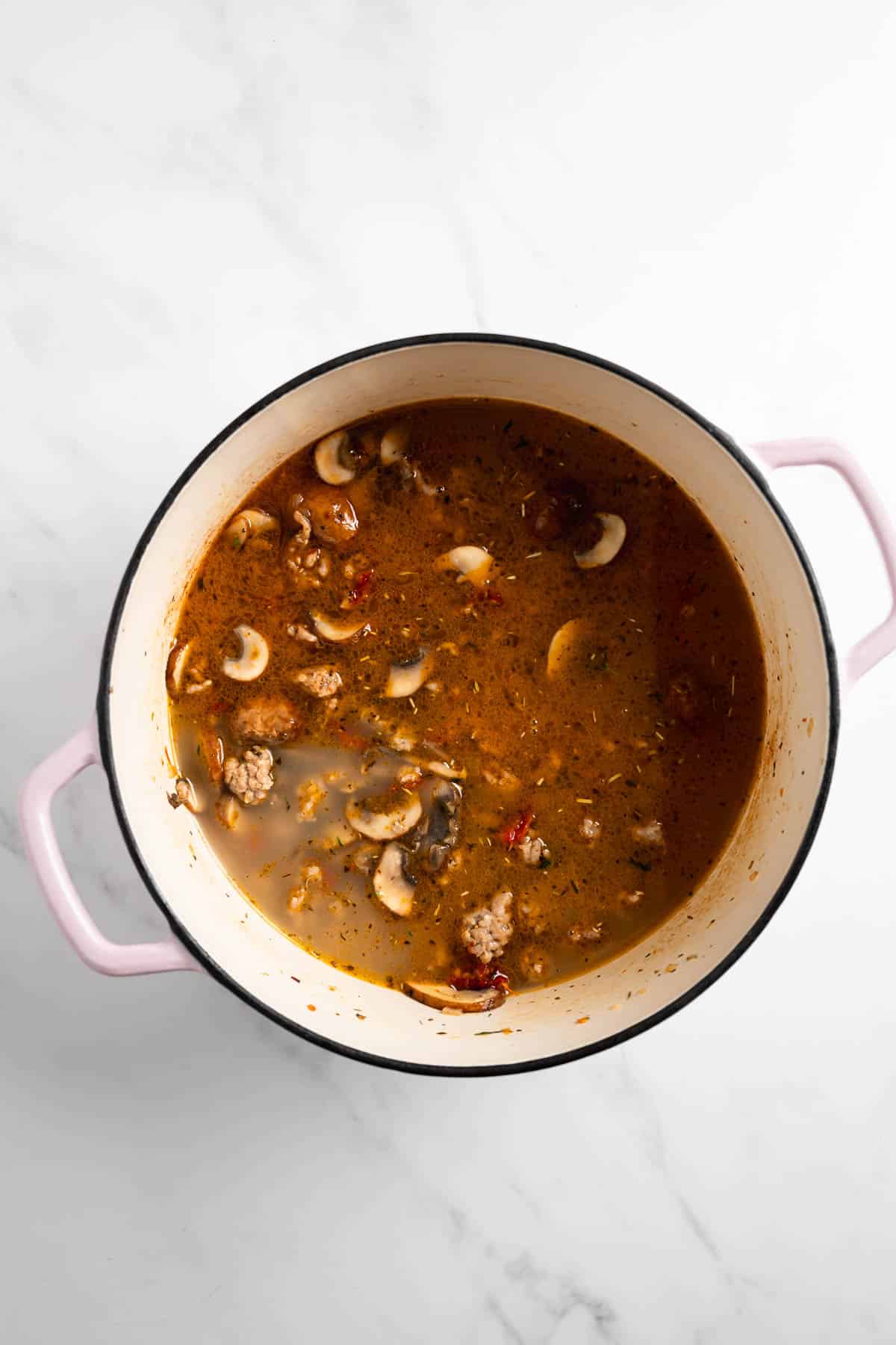 chicken broth combined with sausage and vegetables in a pot.