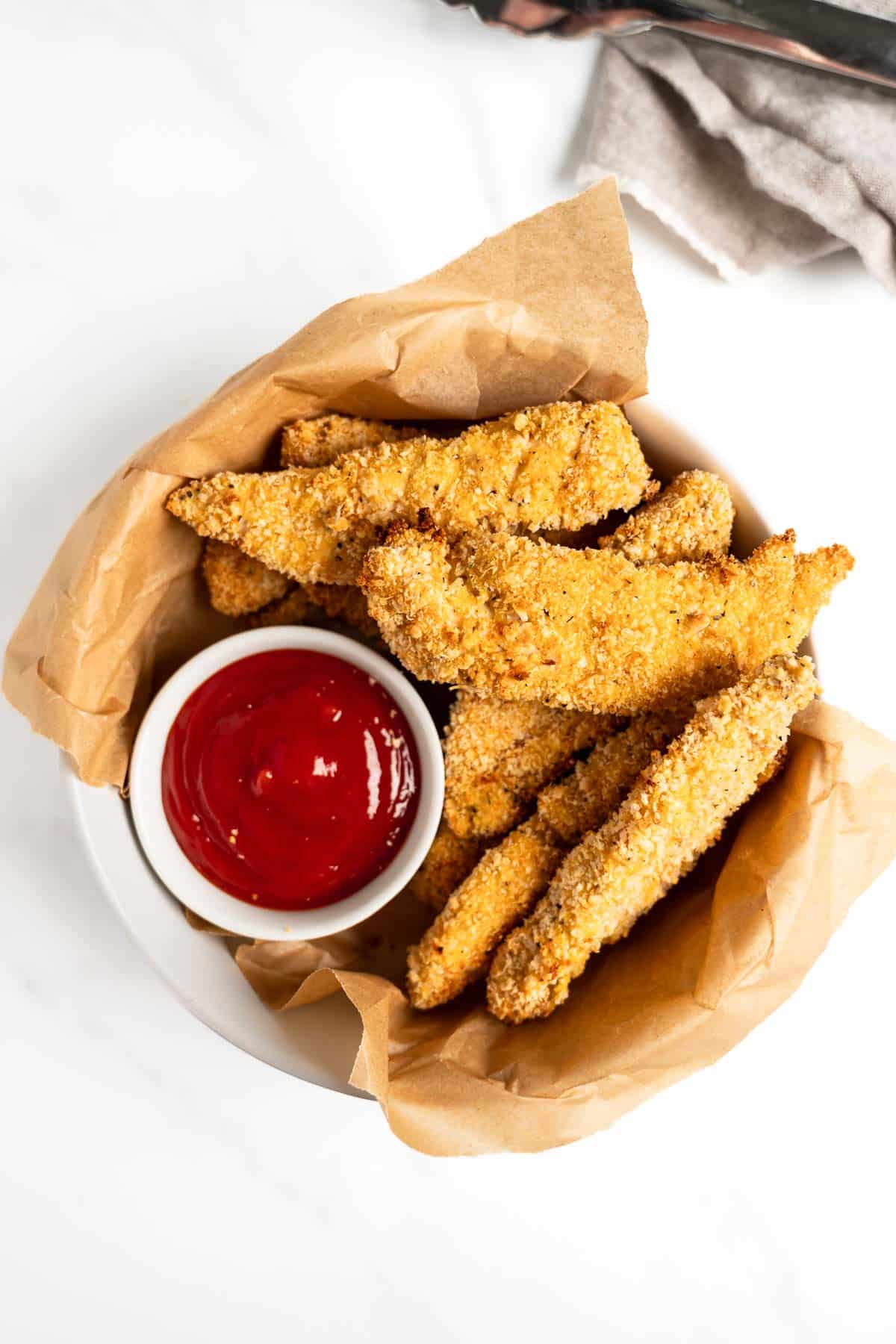 crispy baked chicken tenders in a bowl with ketchup.