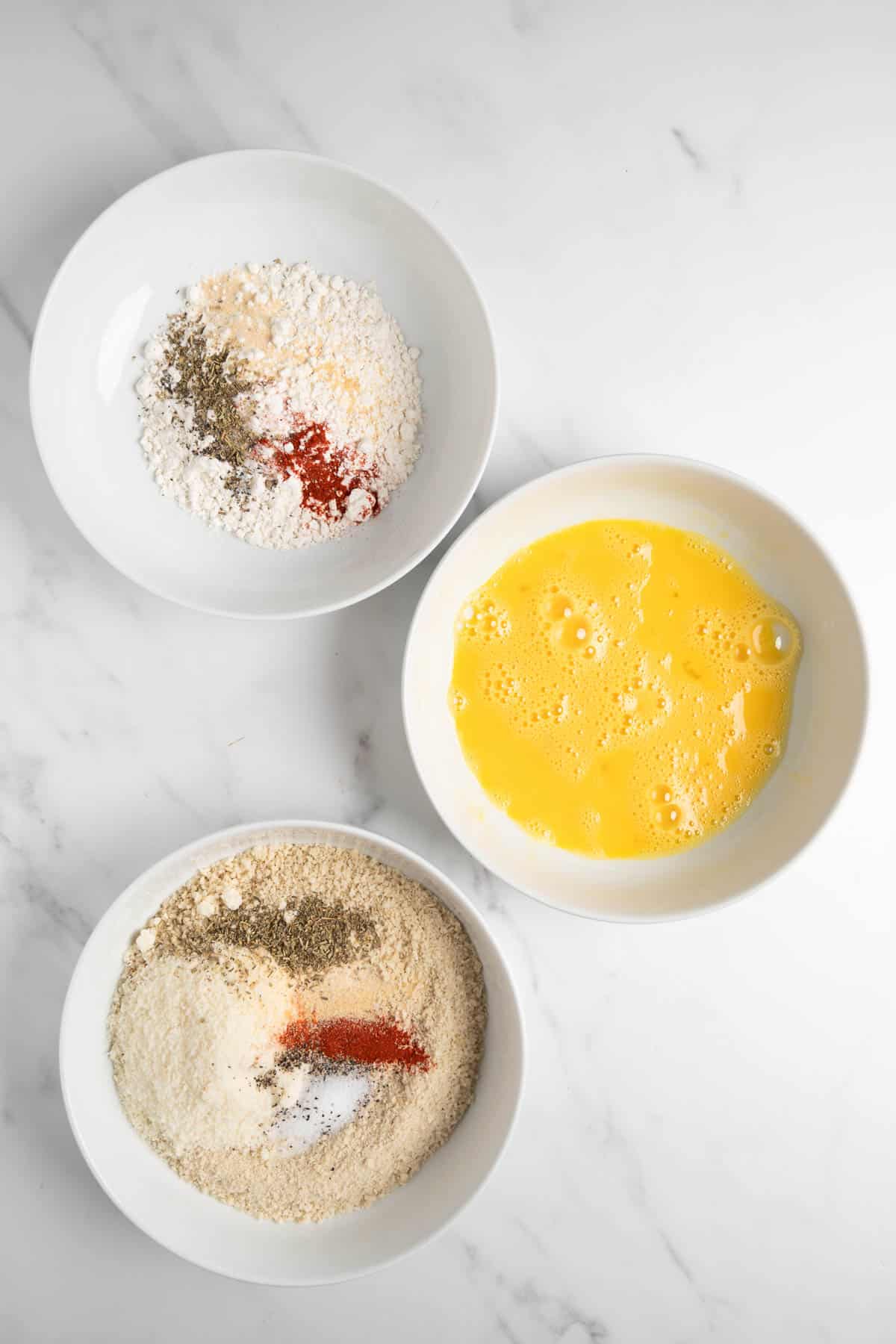 three bowls on a table with flour, egg, and panko breadcrumb with spices.