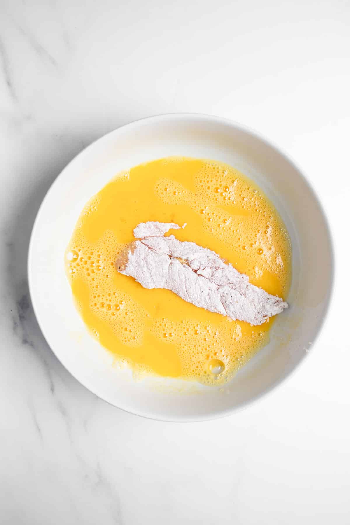 chicken being dipped in a bowl with egg.