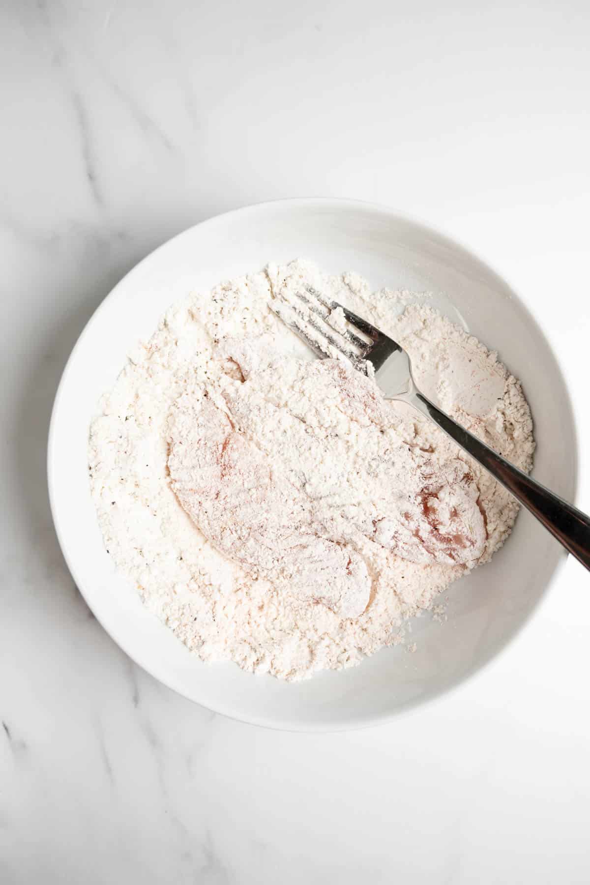 chicken coated in flour in a bowl with a fork.