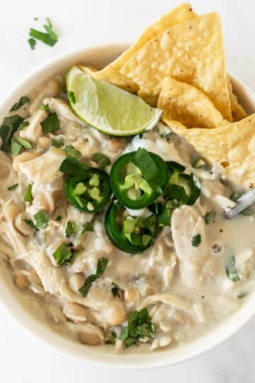 white chicken chili in a bowl topped with jalapeños, lime, and chips.