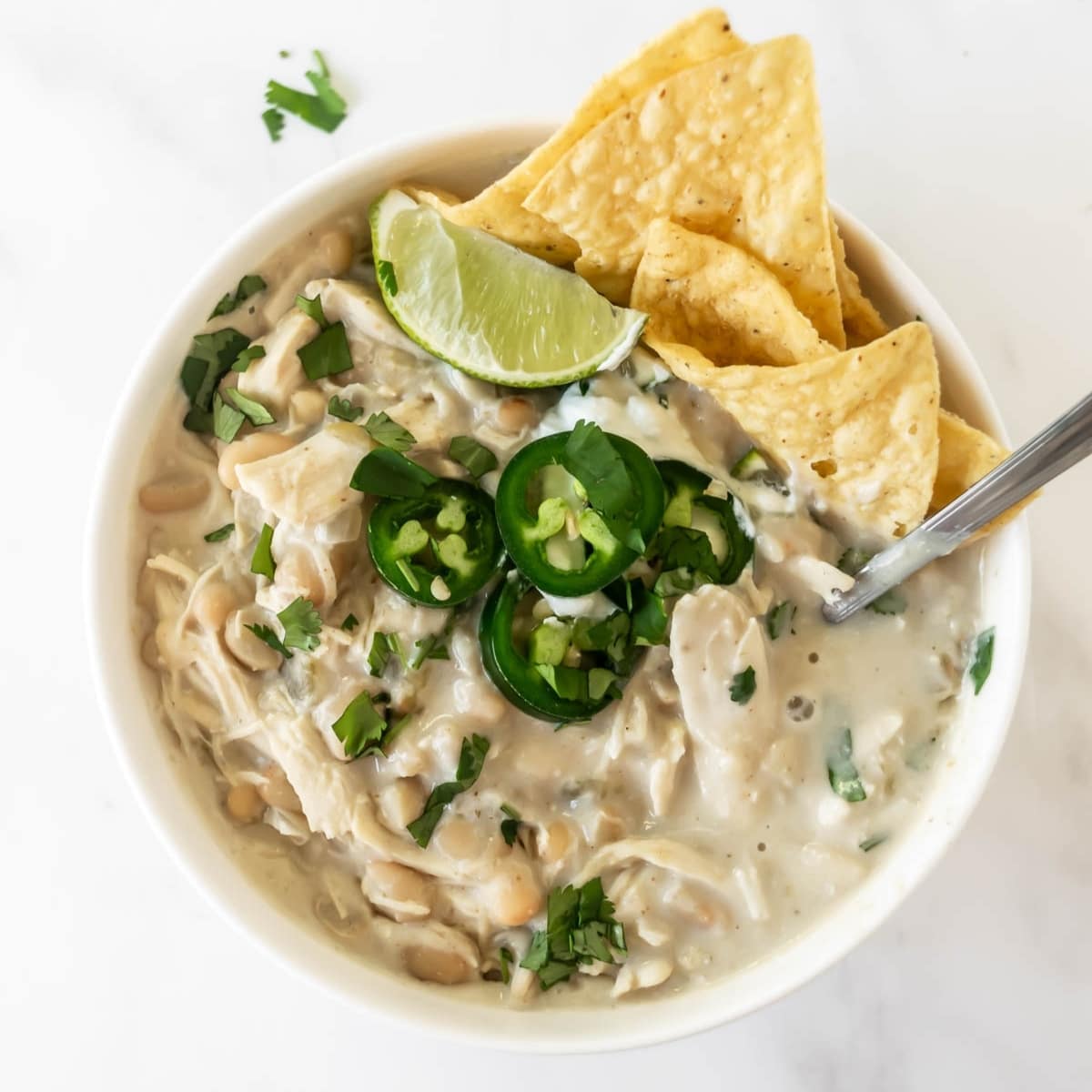 white chicken chili in a bowl topped with jalapeños, lime, and chips.