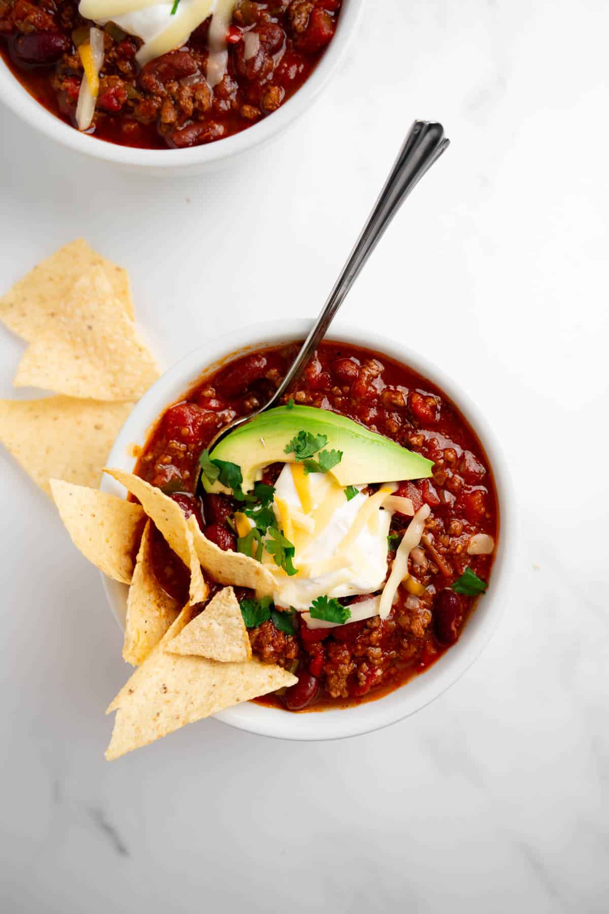 homemade chili in a bowl with a spoon and toppings.