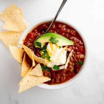 homemade chili in a bowl topped with sour cream, cheese, avocado, and chips.